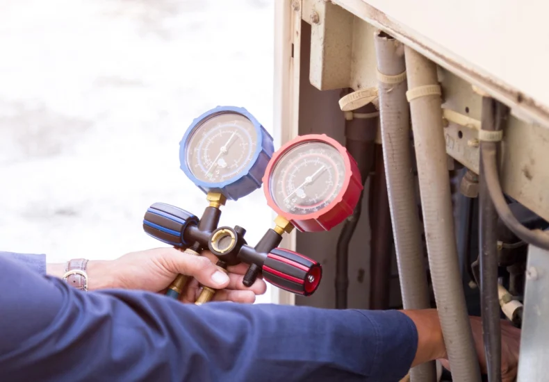 Technician holding HVAC manifold gauges, checking pressure on air conditioning unit with connected hoses.