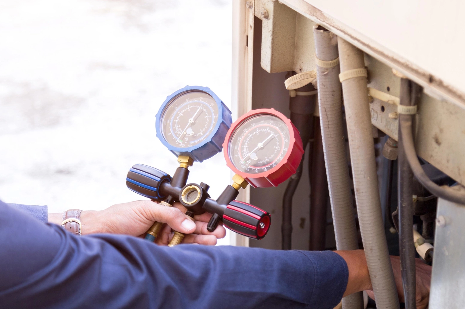 Technician holding HVAC manifold gauges, checking pressure on air conditioning unit with connected hoses.